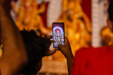 Elleri cep telefonu tutuyor ve Tanrıça Durga idolünün pandalda fotoğraflarını çekiyor. Durga Puja, Bengali cemaatinin en büyük dini bayramıdır..