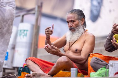 Varanasi, Uttar Pradesh, Hindistan - 18 Ocak 2024: Varanasi 'deki çetelerin yakınındaki ghatlarda oturan geleneksel bir sadhu baba resmi. Sadhu, Kaşhi 'de Ganga yakınlarında meditasyon yapıyor..