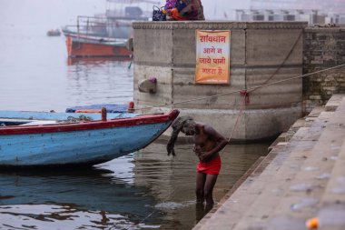 Varanasi, Uttar Pradesh, India - January 18 2024: People on the ghats near ganges in varanasi. Sadhu performs meditation near ganga in kashi. clipart