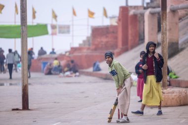 Varanasi, Uttar Pradesh, Hindistan - 18 Ocak 2024: Gurukul okulunun Hintli öğrencileri kış sabahı arkadaşlarıyla birlikte Varanasi 'de nehir keneviri ghatlarında kriket oynuyorlar.