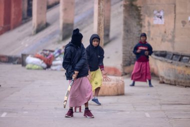 Varanasi, Uttar Pradesh, Hindistan - 18 Ocak 2024: Gurukul okulunun Hintli öğrencileri kış sabahı arkadaşlarıyla birlikte Varanasi 'de nehir keneviri ghatlarında kriket oynuyorlar.