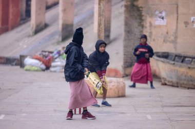 Varanasi, Uttar Pradesh, Hindistan - 18 Ocak 2024: Gurukul okulunun Hintli öğrencileri kış sabahı arkadaşlarıyla birlikte Varanasi 'de nehir keneviri ghatlarında kriket oynuyorlar.