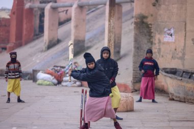 Varanasi, Uttar Pradesh, Hindistan - 18 Ocak 2024: Gurukul okulunun Hintli öğrencileri kış sabahı arkadaşlarıyla birlikte Varanasi 'de nehir keneviri ghatlarında kriket oynuyorlar.