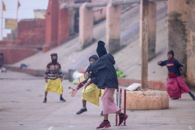 Varanasi, Uttar Pradesh, Hindistan - 18 Ocak 2024: Gurukul okulunun Hintli öğrencileri kış sabahı arkadaşlarıyla birlikte Varanasi 'de nehir keneviri ghatlarında kriket oynuyorlar.