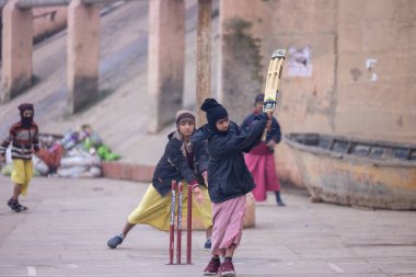Varanasi, Uttar Pradesh, Hindistan - 18 Ocak 2024: Gurukul okulunun Hintli öğrencileri kış sabahı arkadaşlarıyla birlikte Varanasi 'de nehir keneviri ghatlarında kriket oynuyorlar.