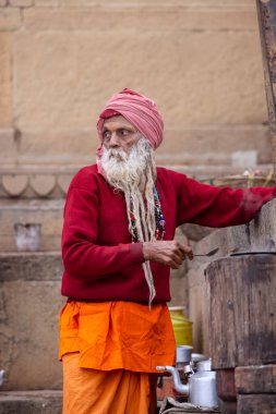 Varanasi, Uttar Pradesh, Hindistan - 18 Ocak 2024: Varanasi 'de kış sabahı nehir keneviri yakınlarında çay hazırlayan yaşlı bir sadhu sokak satıcısının portresi.