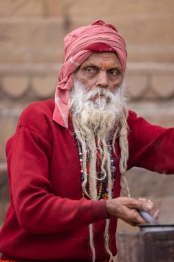 Varanasi, Uttar Pradesh, Hindistan - 18 Ocak 2024: Varanasi 'de kış sabahı nehir keneviri yakınlarında çay hazırlayan yaşlı bir sadhu sokak satıcısının portresi.
