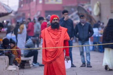 Varanasi, Uttar Pradesh, Hindistan - 19 Ocak 2024: Varanasi 'deki çetelerin yakınındaki ghatlarda yürüyen geleneksel sadhu elbiseli yaşlı bir adamın portresi.