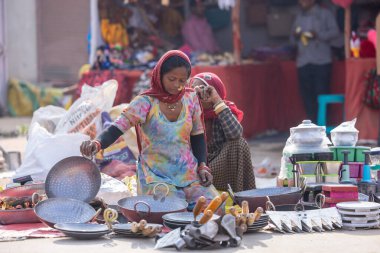 Puşkar, Rajasthan, Hindistan - 25 Kasım 2023: Puşkar Fuarı, Rajasthan 'lı Hintli bir kadının portresi, geleneksel renkli elbiseler ve başörtüsü ile sokak fuarında ürünler satışı.