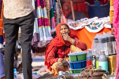 Puşkar, Rajasthan, Hindistan - 25 Kasım 2023: Puşkar Fuarı, Rajasthan 'lı Hintli bir kadının portresi, geleneksel renkli elbiseler ve başörtüsü ile sokak fuarında ürünler satışı.