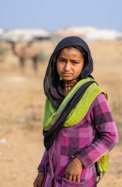 Puşkar, Rajasthan, Hindistan - 25 Kasım 2023: Pushkar Deve Fuarı 'nda kış sabahı renkli geleneksel elbiseler giyen Hintli genç bir kadının portresi.