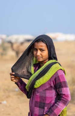 Puşkar, Rajasthan, Hindistan - 25 Kasım 2023: Pushkar Deve Fuarı 'nda kış sabahı renkli geleneksel elbiseler giyen Hintli genç bir kadının portresi.