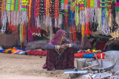 Puşkar, Rajasthan, Hindistan - 25 Kasım 2023: Puşkar Fuarı, Rajasthan 'lı Hintli bir kadının portresi, geleneksel renkli elbiseler ve başörtüsü ile sokak fuarında ürünler satışı.