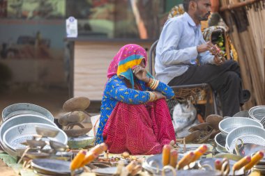 Puşkar, Rajasthan, Hindistan - 25 Kasım 2023: Puşkar Fuarı, Rajasthan 'lı Hintli bir kadının portresi, geleneksel renkli elbiseler ve başörtüsü ile sokak fuarında ürünler satışı.