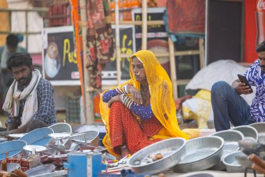 Puşkar, Rajasthan, Hindistan - 25 Kasım 2023: Puşkar Fuarı, Rajasthan 'lı Hintli bir kadının portresi, geleneksel renkli elbiseler ve başörtüsü ile sokak fuarında ürünler satışı.