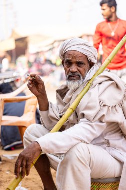 Puşkar, Rajasthan, Hindistan - 25 Kasım 2023: Puşkar Fuarı, Rajasthan 'lı Hintli bir kadının portresi, geleneksel renkli elbiseler ve başörtüsü ile sokak fuarında ürünler satışı.