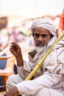 Puşkar, Rajasthan, Hindistan - 25 Kasım 2023: Puşkar Fuarı, Rajasthan 'lı Hintli bir kadının portresi, geleneksel renkli elbiseler ve başörtüsü ile sokak fuarında ürünler satışı.