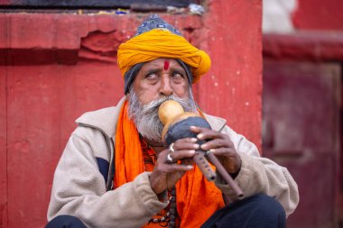 Kimliği belirsiz yaşlı bir yılan oynatıcısının portresi Varanasi şehrinde yılanla nehir kenarında gösteri yapıyor ve turistleri kendine çekiyor.
