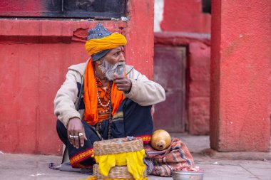Kimliği belirsiz yaşlı bir yılan oynatıcısının portresi Varanasi şehrinde yılanla nehir kenarında gösteri yapıyor ve turistleri kendine çekiyor.