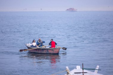 Varanasi, Uttar Pradesh, Hindistan - 19 Ocak 2024: Turistler sabahın erken saatlerinde Varanasi 'deki nehir çetelerinde tekne turunun keyfini çıkarıyorlar. Kayıkçı kışın sisli sabahında tahta teknede yelken açıyor..