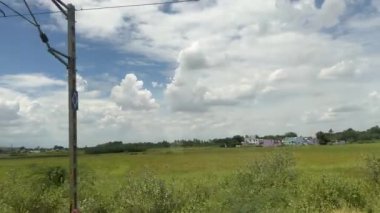 Tirunelveli, Tamilnadu, Hindistan - 13 Ekim 2024: Tarım arazilerinin dikey modunda manzara, tren penceresinden beyaz bulutlar geçen mavi gökyüzünün altında tren yolu.