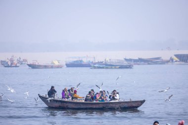 Varanasi, Uttar Pradesh, Hindistan - 19 Ocak 2024: Turistler sabahın erken saatlerinde Varanasi 'deki nehir çetelerinde tekne turunun keyfini çıkarıyorlar. Kayıkçı kışın sisli sabahında tahta teknede yelken açıyor..