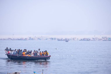 Varanasi, Uttar Pradesh, Hindistan - 19 Ocak 2024: Turistler sabahın erken saatlerinde Varanasi 'deki nehir çetelerinde tekne turunun keyfini çıkarıyorlar. Kayıkçı kışın sisli sabahında tahta teknede yelken açıyor..