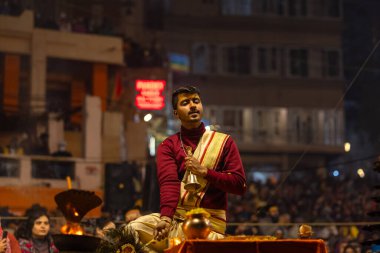Varanasi, Uttar Pradesh, Hindistan - 19 Ocak 2024: Ganga aarti, Dashashwamedh ghat geleneksel elbise ve Hindu ayinleri ile kutsal nehir keneviri akşam ayini yapan genç bir rahibin portresi.