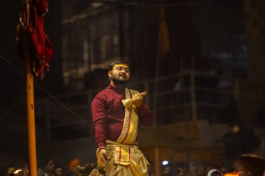 Varanasi, Uttar Pradesh, Hindistan - 19 Ocak 2024: Ganga aarti, Dashashwamedh ghat geleneksel elbise ve Hindu ayinleri ile kutsal nehir keneviri akşam ayini yapan genç bir rahibin portresi.