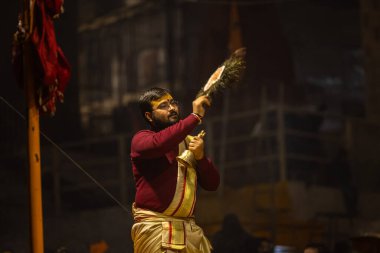 Varanasi, Uttar Pradesh, Hindistan - 19 Ocak 2024: Ganga aarti, Dashashwamedh ghat geleneksel elbise ve Hindu ayinleri ile kutsal nehir keneviri akşam ayini yapan genç bir rahibin portresi.