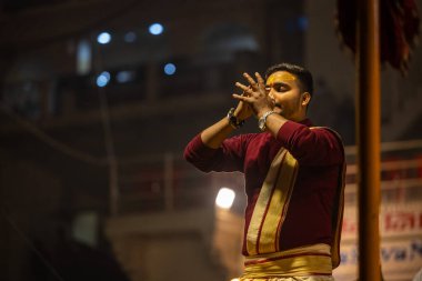 Varanasi, Uttar Pradesh, Hindistan - 19 Ocak 2024: Ganga aarti, Dashashwamedh ghat geleneksel elbise ve Hindu ayinleri ile kutsal nehir keneviri akşam ayini yapan genç bir rahibin portresi.