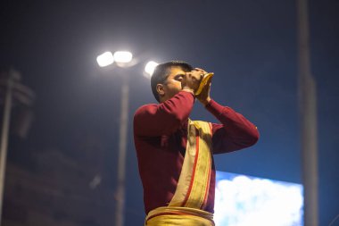 Varanasi, Uttar Pradesh, Hindistan - 19 Ocak 2024: Ganga aarti, Dashashwamedh ghat geleneksel elbise ve Hindu ayinleri ile kutsal nehir keneviri akşam ayini yapan genç bir rahibin portresi.