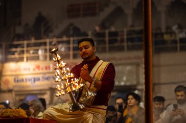 Varanasi, Uttar Pradesh, Hindistan - 19 Ocak 2024: Ganga aarti, Dashashwamedh ghat geleneksel elbise ve Hindu ayinleri ile kutsal nehir keneviri akşam ayini yapan genç bir rahibin portresi.