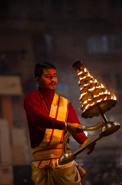 Varanasi, Uttar Pradesh, Hindistan - 19 Ocak 2024: Ganga aarti, Dashashwamedh ghat geleneksel elbise ve Hindu ayinleri ile kutsal nehir keneviri akşam ayini yapan genç bir rahibin portresi.