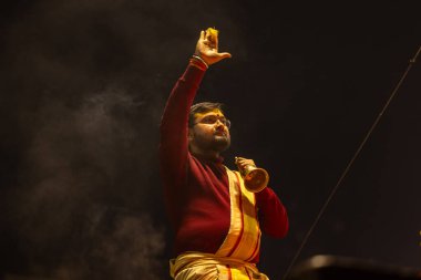 Varanasi, Uttar Pradesh, Hindistan - 19 Ocak 2024: Ganga aarti, Dashashwamedh ghat geleneksel elbise ve Hindu ayinleri ile kutsal nehir keneviri akşam ayini yapan genç bir rahibin portresi.