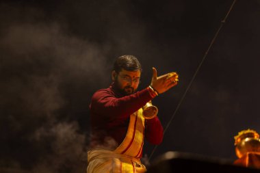 Varanasi, Uttar Pradesh, Hindistan - 19 Ocak 2024: Ganga aarti, Dashashwamedh ghat geleneksel elbise ve Hindu ayinleri ile kutsal nehir keneviri akşam ayini yapan genç bir rahibin portresi.