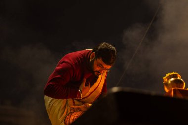 Varanasi, Uttar Pradesh, Hindistan - 19 Ocak 2024: Ganga aarti, Dashashwamedh ghat geleneksel elbise ve Hindu ayinleri ile kutsal nehir keneviri akşam ayini yapan genç bir rahibin portresi.