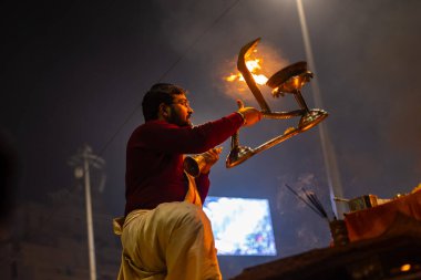 Varanasi, Uttar Pradesh, Hindistan - 19 Ocak 2024: Ganga aarti, Dashashwamedh ghat geleneksel elbise ve Hindu ayinleri ile kutsal nehir keneviri akşam ayini yapan genç bir rahibin portresi.
