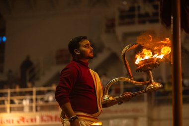 Varanasi, Uttar Pradesh, Hindistan - 19 Ocak 2024: Ganga aarti, Dashashwamedh ghat geleneksel elbise ve Hindu ayinleri ile kutsal nehir keneviri akşam ayini yapan genç bir rahibin portresi.
