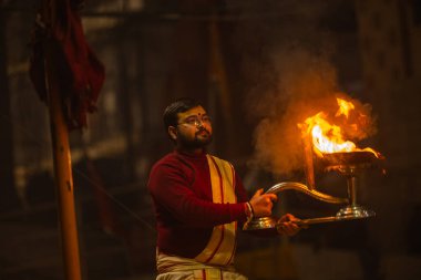 Varanasi, Uttar Pradesh, Hindistan - 19 Ocak 2024: Ganga aarti, Dashashwamedh ghat geleneksel elbise ve Hindu ayinleri ile kutsal nehir keneviri akşam ayini yapan genç bir rahibin portresi.