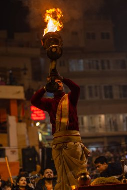 Varanasi, Uttar Pradesh, Hindistan - 19 Ocak 2024: Ganga aarti, Dashashwamedh ghat geleneksel elbise ve Hindu ayinleri ile kutsal nehir keneviri akşam ayini yapan genç bir rahibin portresi.