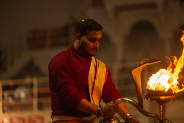 Varanasi, Uttar Pradesh, Hindistan - 19 Ocak 2024: Ganga aarti, Dashashwamedh ghat geleneksel elbise ve Hindu ayinleri ile kutsal nehir keneviri akşam ayini yapan genç bir rahibin portresi.