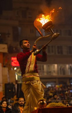 Varanasi, Uttar Pradesh, Hindistan - 19 Ocak 2024: Ganga aarti, Dashashwamedh ghat geleneksel elbise ve Hindu ayinleri ile kutsal nehir keneviri akşam ayini yapan genç bir rahibin portresi.