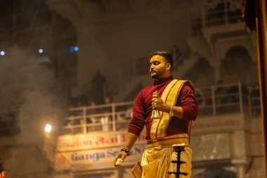 Varanasi, Uttar Pradesh, Hindistan - 19 Ocak 2024: Ganga aarti, Dashashwamedh ghat geleneksel elbise ve Hindu ayinleri ile kutsal nehir keneviri akşam ayini yapan genç bir rahibin portresi.