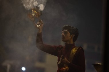 Varanasi, Uttar Pradesh, India - January 20 2024: Ganga aarti, Portrait of a young male hindu priest performing holy river ganga early morning aarti at assi ghat in traditional dress with rituals. clipart