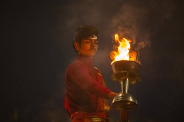 Varanasi, Uttar Pradesh, Hindistan - 20 Ocak 2024: Ganga aarti, genç bir Hindu papazın portresi sabahın erken saatlerinde Assi Ghat 'ta geleneksel ayinlerle geleneksel kıyafetlerle Ganga nehri aarti sergiliyor..