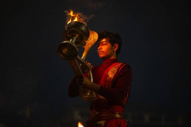 Varanasi, Uttar Pradesh, Hindistan - 20 Ocak 2024: Ganga aarti, genç bir Hindu papazın portresi sabahın erken saatlerinde Assi Ghat 'ta geleneksel ayinlerle geleneksel kıyafetlerle Ganga nehri aarti sergiliyor..