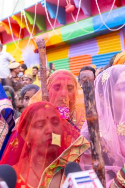 Barsana, Uttar Pradesh, Hindistan - 18 Mart 2024: Geleneksel barsana elbiseli Hindu kadın grubu Nandgaon 'dan erkeklere vurmak için bambu çubuklarla duruyorlar..