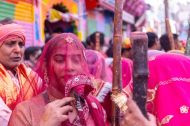 Barsana, Uttar Pradesh, Hindistan - 18 Mart 2024: Geleneksel barsana elbiseli Hindu kadın grubu Nandgaon 'dan erkeklere vurmak için bambu çubuklarla duruyorlar..