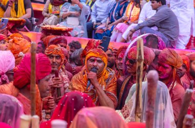 Barsana, Uttar Pradesh, India - March 18, 2024: Group of hindu male from nandgaon in traditional clothes and colorful faces celebrating the lathmar holi in rangili gali of barsana with tradition. clipart